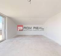An empty room with balcony doors in a family house, also showing the sky and roofs.
