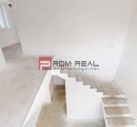 A staircase in a family house with white walls and an unfinished floor.
