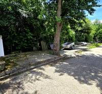 A trailer and car area among trees around warehouses and halls of Banská Bystrica.