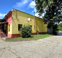 A yellow building with metal stairs, next to it trees, surrounded by greenery in warehouses and halls.
