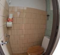 A toilet in a 2-room apartment with a wooden seat and beige tiles.