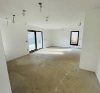 Interior of a family house with a concrete floor and large windows providing a view of the garden.