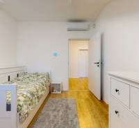 A room in a 5 or more bedroom apartment with a bed, a dresser, and wooden flooring.