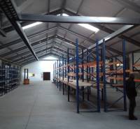 There are empty shelves in the warehouse and a person is standing by them.