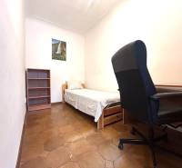 A room in a 3-room apartment with a bed, chair, shelf, and a picture on the wall.