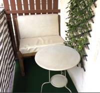 A balcony in a 3-room apartment with a chair, table, and vertical greenery on the wall.