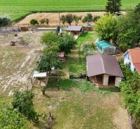 A garden in Kolárovo by a family house with shelters and a greenhouse surrounded by fields.