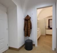 The hallway in a 2-room apartment with a wooden floor, a coat on the hanger, and open doors to the bathroom.