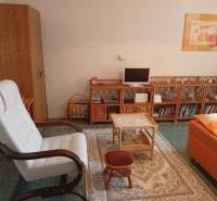 Living area of a studio apartment with a comfortable armchair, bookshelf, and carpet.