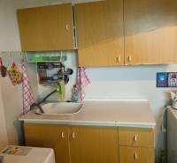 A kitchen in a studio apartment with a sink, a kettle, and decorations on the wall.