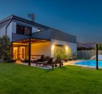 A family house in Kvetoslavov with a lit terrace, lawn, and pool at sunset.