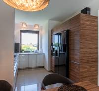 A kitchen in a family house with wooden cabinets, a black refrigerator, and a large window.