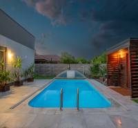 A family house in Kvetoslavov with a lit swimming pool, paving, and a wooden sauna in the garden.