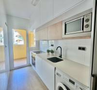 The kitchen in the vacation apartment, equipped with appliances, a sink, and white cabinets, with access to the balcony.