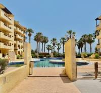 A holiday apartment in Los Alcázares with a pool, palm trees, and yellow buildings in a sunny location.