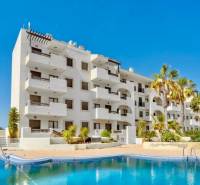 Recreational apartment in Los Alcázares with a pool, palm trees, and blue sky.