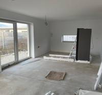 An interior under construction with a large window, space for a kitchen, and a concrete floor.