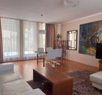Living room with wooden flooring and a sofa in a three-room apartment, large windows with delicate curtains.