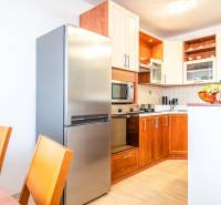 A kitchen in a 3-room apartment with wooden cabinets, a refrigerator, and a fruit bowl on the table.