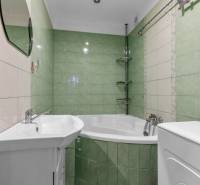 A bathroom in a 3-room apartment with a corner bathtub and green tiles.