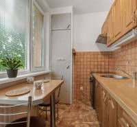 The kitchen of a three-room apartment with a wooden cabinet and a large window with internal blinds.