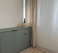 A green cabinet with decoration in a studio apartment by a white curtain and wall.