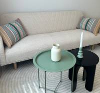 A white sofa with striped cushions, a green and black table in a studio apartment.
