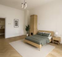 A bright bedroom with a wooden floor, a bed, and a tiled stove in a studio apartment.