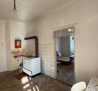 A kitchen with a stove, wooden floor, and a table in a studio apartment with simple furnishings.