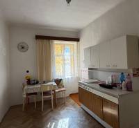 A kitchen in a studio apartment with a wooden floor, table, and cabinets.