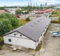 A building with a parking lot surrounded by greenery, buses in the background, and Bratislava - Nové Mesto.