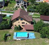 A family house in Vyšná Myšľa with a pool in the garden, surrounded by greenery and nearby houses.