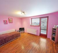 A room in a family house, pink walls, wooden floor, bed, television, and shelves.