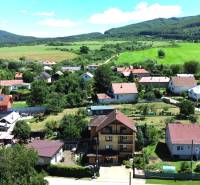 Aerial view of family houses in the village of Vyšná Myšľa surrounded by green fields and hills.