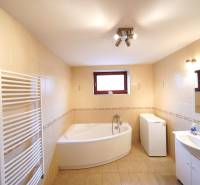 Bathroom in a family house with a bathtub, sink, washing machine, and mirror.