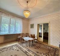 A room in a family house with a chandelier, carved floor, carpet, and a large window.