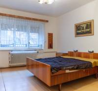 Bedroom of a family house with a wooden bed, a row of wardrobes, and a large window.