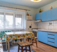 A kitchen in a family house with blue cabinets, a dining table, and large windows.
