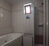 A bathroom in a family house with tiles, a bathtub, and a shower corner.