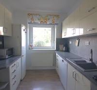 A kitchen in a family house with white cabinets, a large window, and appliances.