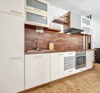 A kitchen in a 3-room apartment with wooden flooring and white and brown cabinets.