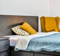 Bedroom with a bed and a nightstand in a 3-room apartment, yellow chair in the corner.