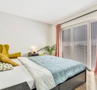A bedroom with a yellow armchair, a bed, and pink curtains in a three-room apartment.
