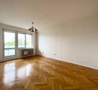 A spacious room with wooden flooring and a large window in a 2-room apartment.