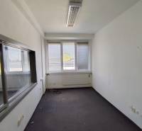An empty office space with a window and radiator, ready for rent.