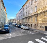 A narrow city street with parked cars, sidewalks, and older buildings.