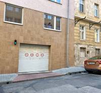 A gate in the city center with traffic signs and a brown car, garages in the background.