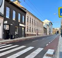 A street with a crosswalk, historic buildings, and a blue sky. Traffic signs, a bicycle path, and garages.