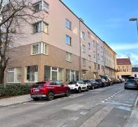 A street with cars, buildings, trees, in the background a blue sky and parked garages.