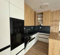 A modern kitchen with white cabinets and built-in appliances in a three-room apartment.